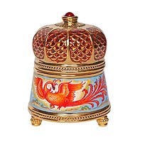 Музыкальная шкатулка Жар-птица. Металл, эмаль, деколь, House of Faberge, 1990-е гг.шк.ал.121 Музыкальная шкатулка Жар-птица. Металл, эмаль, деколь, House of Faberge, 1990-е гг.шк.ал.121Музыкальная шкатулка Жар-птица. Металл, эмаль, деколь. Западная Европа, Фаберже, 1990-е гг. Высота 9,5 см, диаметр 7 см. Сохранность хорошая. На дне находится заводной ключик шкатулки, там же золотая марки Firebird, Ф. На тулове шкатулки воспроизводятся сценки из сказки Жар-птица: крупная яркая Жар-птица, герой сказки (Иван-царевич, вероятно), поймавший ее за хвост. Третий сюжет посвящен изображению райского сада с золотыми яблоками, где жила чудо-птица. Золоченая крышка шкатулки выполнена в виде купола и украшена крупным красным стразом.