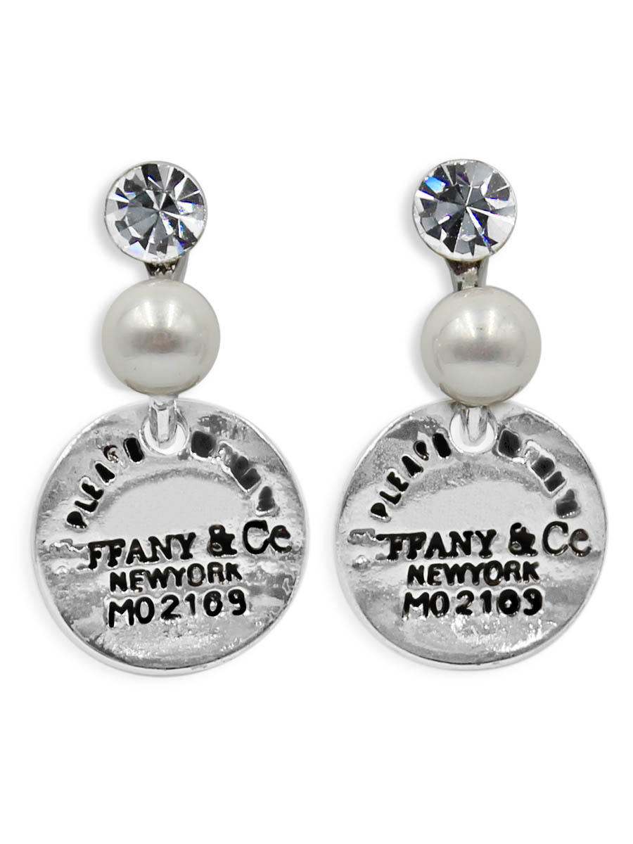 Серьги Taya, цвет: серебристый. T-B-12359T-B-12359-EARR-SILVER Серьги Taya, цвет: серебристый. T-B-12359T-B-12359-EARR-SILVERСерьги-гвоздики с заглушкой металл-пластик изготовлены из бижутерного сплава. С одной стороны скобы кристалл, с другой оформлена мелкая жемчужина. Снизу подвижно крепится монетка с надписями.