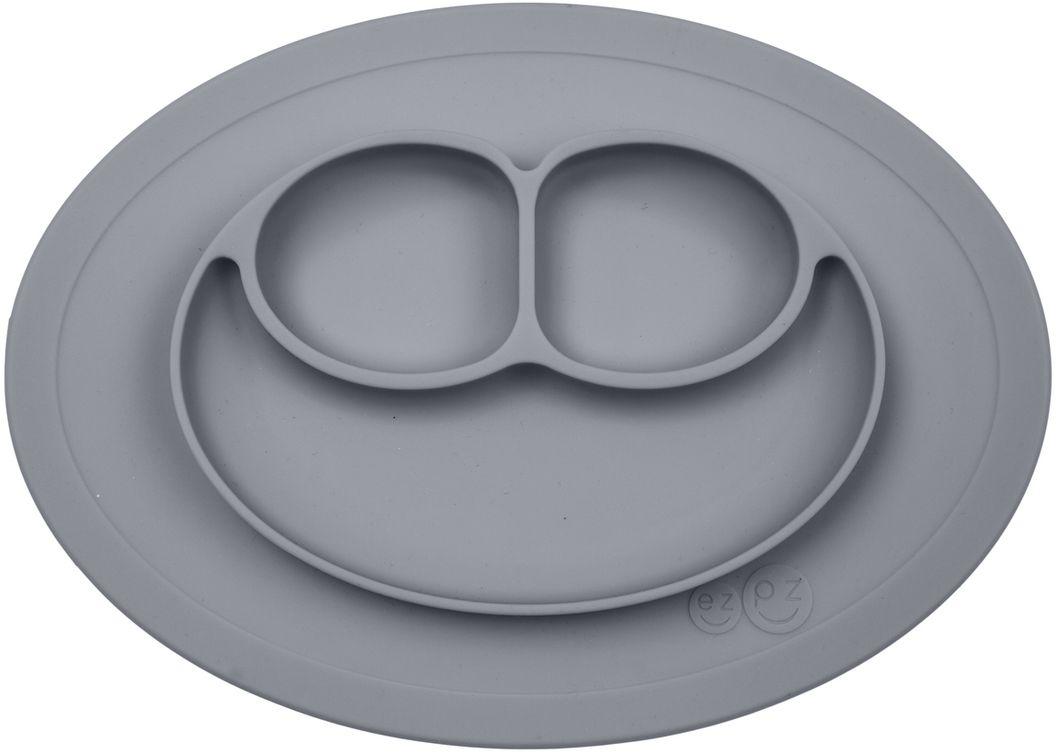 Ezpz Тарелка детская Mini Mat цвет серый115510 Ezpz Тарелка детская Mini Mat цвет серый115510Ezpz Mini Mat - уменьшенная версия тарелочки-плейсмата Happy Mat. Предназначена для столиков для кормления и использования в поездках. Рекомендована для малышей от 4 месяцев. Тарелка тоньше, легче и компактнее, чем Happy Mat, но обладает теми же отличительными чертами: присасывается к столу, чтобы ребенок не смог ее перевернуть; подходит для микроволновки и посудомоечной машины; улыбается и вызывает у детей улыбку. Вмещает 240 мл. У тарелочки также есть удобный чехольчик с ручками, который легко можно взять с собой.Тарелка разработана и запатентована в США. Идея создания удобной безопасной посуды для детей принадлежит многодетной маме, которая как никто другой знает, как сложно уследить за детками во время еды и сохранить при этом чистоту и порядок. Благодаря такой тарелочке прием пищи становится веселым и безопасным, а кухня остается чистой и опрятной.